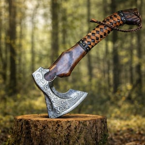 May include: A handcrafted axe with a silver blade featuring intricate engraved designs. The wooden handle is stained a dark brown and wrapped with a woven leather grip. The axe is displayed on a moss-covered tree stump against a blurred forest backdrop.