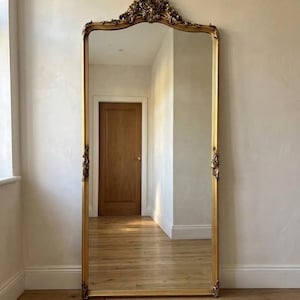Sierlijke gouden vloerspiegel in barokstijl over de hele lengte met decoratief embleem