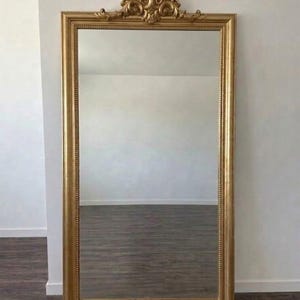 Sierlijke gouden vloerspiegel in barokstijl over de hele lengte met decoratief embleem