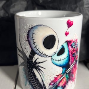 May include: White ceramic mug featuring a colorful illustration of Jack Skellington and Sally from The Nightmare Before Christmas. The design includes hearts and a romantic embrace, perfect for fans of the movie.