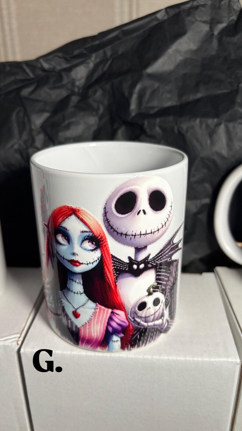 May include: White ceramic mug featuring Jack Skellington and Sally from The Nightmare Before Christmas. Sally has red hair and a stitched appearance. Jack has a skeletal face. A small pumpkin is also featured on the mug.