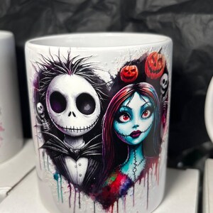 May include: White ceramic mug featuring a heart-shaped design with Jack Skellington and Sally from The Nightmare Before Christmas. The design includes pumpkins, skulls, and a watercolor effect. The letter "E." is visible on the mug.