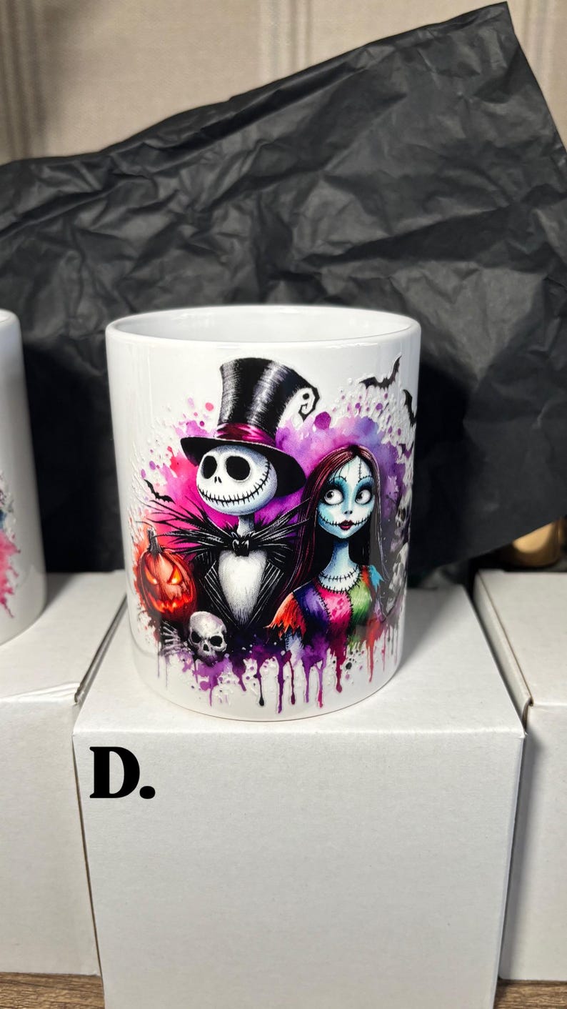 May include: White ceramic mug featuring Jack Skellington and Sally from The Nightmare Before Christmas, with a pumpkin and skull. The design includes a black top hat, bats, and colorful paint splatters. A Halloween-themed item.