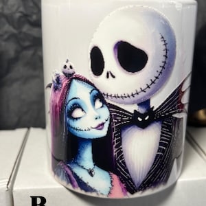 May include: White ceramic mug featuring Jack Skellington and Sally from The Nightmare Before Christmas. Jack is in a black suit with a bat-shaped bow tie, and Sally has blue skin and pink hair. The mug has the letter "B." on the bottom.