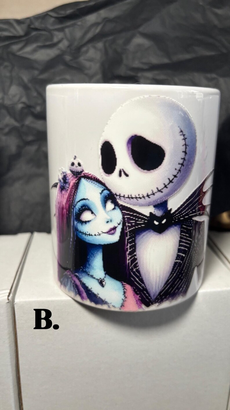 May include: White ceramic mug featuring Jack Skellington and Sally from The Nightmare Before Christmas. Jack is in a black suit with a bat-shaped bow tie, and Sally has blue skin and pink hair. The mug has the letter "B." on the bottom.