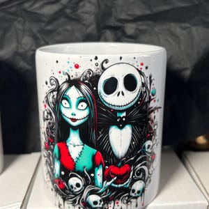 May include: White ceramic mug featuring a colorful illustration of Jack Skellington and Sally from The Nightmare Before Christmas. The design includes skulls, hearts, and a spooky aesthetic. The letter "C." is printed on the side.