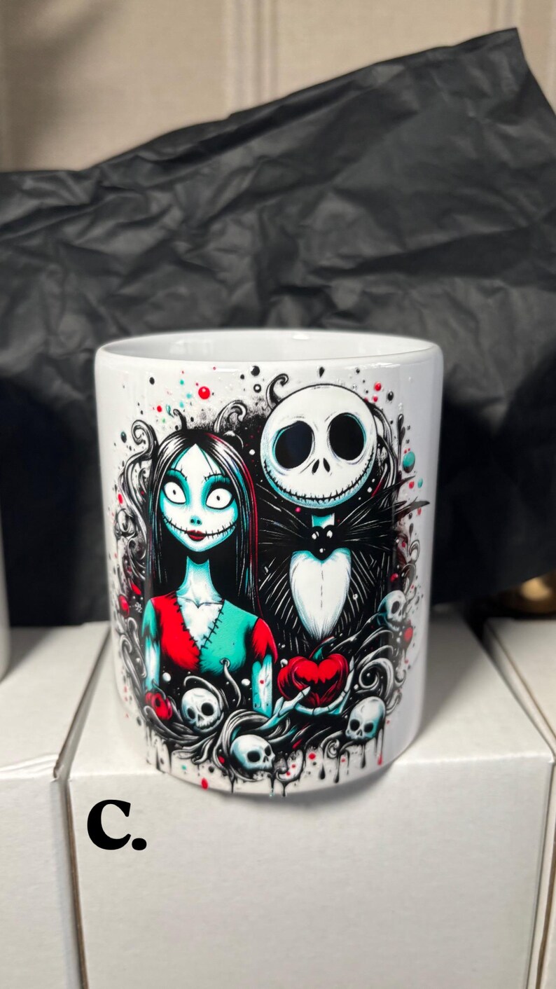 May include: White ceramic mug featuring a colorful illustration of Jack Skellington and Sally from The Nightmare Before Christmas. The design includes skulls, hearts, and a spooky aesthetic. The letter "C." is printed on the side.