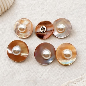 May include: Five circular buttons featuring a polished, iridescent brown shell base with a centered, smooth white pearl-like bead. One button is flipped over to reveal a silver-toned metal shank attachment on the back, while the others show the front.