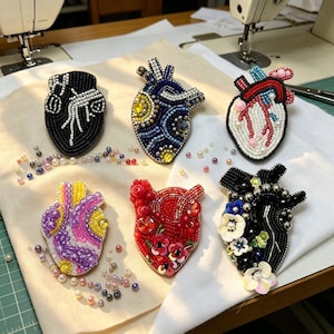 May include: A collection of six beaded heart-shaped brooches. Each brooch features intricate beadwork in various colors, including black, blue, red, and purple. Some are adorned with floral and pearl accents, showcasing detailed craftsmanship.
