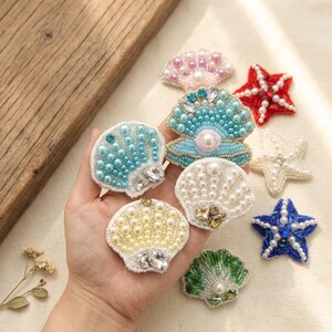 May include: A collection of beaded seashell and starfish embellishments in various colors. The shells feature pearl beads and crystal accents. The starfish are red, white, and blue. These decorative items are ideal for crafting and adding a nautical theme.