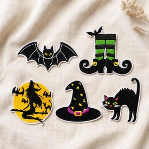 May include: Five embroidered patches featuring Halloween themes: a black bat, a pair of green and black striped witch legs with curled boots, a yellow moon with a black witch silhouette, a black pointed hat with stars, and a black arched cat.