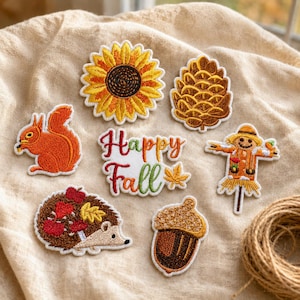 May include: A collection of seven embroidered patches featuring a yellow sunflower, a brown pinecone, an orange squirrel, a scarecrow, a brown hedgehog with red leaves, a brown acorn, and text that reads Happy Fall in red and green.