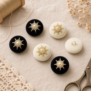 May include: A collection of circular fabric-covered buttons in black and white. Each button features a gold-toned starburst emblem at the center, accented with small clear crystals and a single central faux pearl. One white button shows a plastic shank.