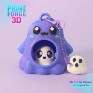 May include: A purple 3D printed ghost-shaped keychain with a hollow centre containing a small white ghost figure. A separate white ghost charm is attached by a purple ball chain. The text PRINT FORGE 3D and Print in Place no supports is visible.