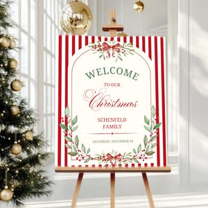 Puede incluir: Un caballete de madera exhibe un letrero de bienvenida con rayas rojas y blancas. El letrero dice "WELCOME to our Christmas" con el apellido y la fecha. El letrero está decorado con hojas verdes y lazos rojos.