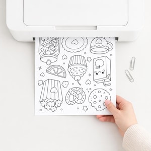 Puede incluir: Una impresora blanca que dispensa una p&aacute;gina para colorear en blanco y negro con ilustraciones de l&iacute;neas de un tarro de dulces, un cupcake, un cart&oacute;n de jugo, un pretzel, una galleta, un recipiente de palomitas y una rodaja de c&iacute;trico.