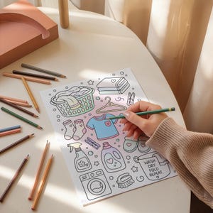 Puede incluir: Una p&aacute;gina para colorear blanca con dibujos lineales sobre el tema de la lavander&iacute;a, incluyendo una cesta, ropa, un pulverizador, una botella de detergente y una lavadora. El texto WASH DRY FOLD REPEAT est&aacute; impreso en un cubo.