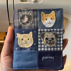 May include: A rectangular fabric patch featuring a patchwork design of blue-toned textiles. It displays three embroidered cat faces, one embroidered pug face, and the white stitched text puiuu on a dark blue square at the bottom right corner.