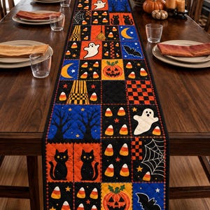 May include: A rectangular quilted table runner featuring a patchwork design with Halloween motifs including ghosts, black cats, pumpkins, bats, spider webs, and candy corn in orange, black, blue, and white colours, laid flat on a wooden dining table.