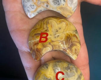 May include: Three polished, crescent-shaped stones with distinctive patterns. Stone A is white, grey, and yellow. Stone B is yellow and brown. Stone C is yellow, grey, and black. Each stone is labelled with a capital letter.
