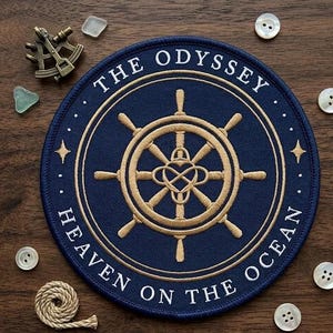 May include: A navy blue circular patch with gold embroidery featuring a ship's wheel design and the words "THE ODYSSEY" and "HEAVEN ON THE OCEAN". The patch is surrounded by white stars and dots. Additional nautical items are scattered around the patch.
