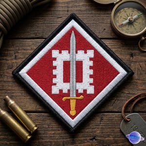 May include: A diamond-shaped patch with a red background, white border, and black trim. The patch features a silver sword with a gold hilt and a white castle-like design. Additional items include a compass, bullets, and a dog tag.