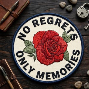 May include: Embroidered patch with a cream background, a red rose, and green leaves. The patch has a navy blue border and the words "NO REGRETS ONLY MEMORIES" in black lettering. The patch is round.