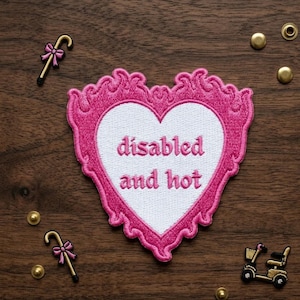 May include: A pink embroidered patch in the shape of a heart with the words "disabled and hot" in pink lettering. The patch is surrounded by a decorative pink border. Also, there are two cane patches with pink bows and a gold scooter patch.