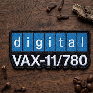 May include: Embroidered patch with the word "digital" in white block letters on a blue background, above "VAX-11/780" in white. The patch is on a wooden surface with cloves and coffee beans.