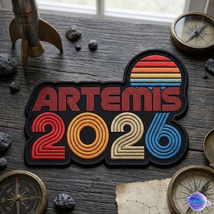 May include: Embroidered patch with the word "ARTEMIS" in red, and the numbers "2026" in red, yellow, and blue. The patch has a retro sunset design and is surrounded by compasses and a toy rocket.