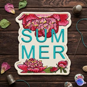 May include: Embroidered patch with the word "SUMMER" in turquoise letters, framed by a cream-colored border. The patch features red and pink peony flowers. Dried petals and sewing notions are scattered around the patch on a wooden surface.