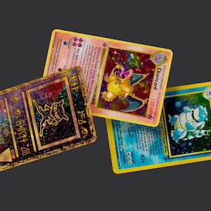 May include: Three Pokémon trading cards: a Charizard card, a Blastoise card, and a Mewtwo card. The Charizard card features a yellow dragon-like creature. The Blastoise card shows a blue turtle-like creature. The Mewtwo card has a gold and black design.