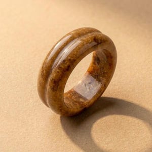 Könnte beinhalten: Nahaufnahme eines braunen Rings mit einem doppelten Rillendesign. Der Ring hat eine polierte, glänzende Oberfläche und scheint aus einem natürlichen Material zu bestehen. Der Ring hat einen warmen, erdigen Ton mit Farbvariationen.