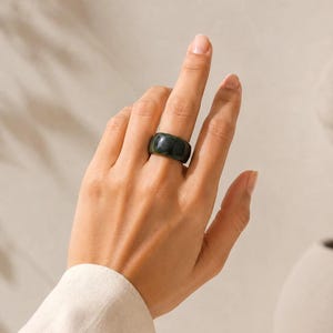 Könnte beinhalten: Ein breiter, glatter Ring in Dunkelgrün mit polierter Oberfläche. Der Ring hat ein massives, abgerundetes Profil und eine tiefe, gleichmäßige waldgrüne Farbe auf der gesamten Oberfläche des Bandes, was eine einfache, durchgehende Kreisform ergibt.