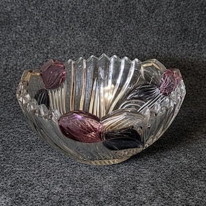 May include: A clear glass bowl with a scalloped rim and a decorative floral design. The bowl features purple, black, and gold accents. The bowl is made of clear glass and has a textured, ribbed exterior.