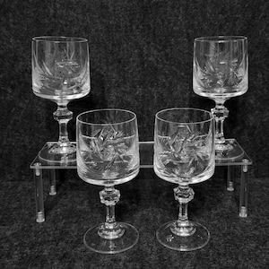 Puede incluir: Cuatro copas de vino de cristal transparente con intrincados patrones de estrella grabados. Dos copas están sobre un soporte de acrílico transparente. Las copas tienen un diseño clásico de cristalería, ideal para servir vino.