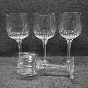 Pode incluir: Um conjunto de quatro taças de vinho de vidro transparente com um padrão de nervuras verticais na metade inferior da taça e um design de haste canelada a condizer. Três taças estão de pé em fila, enquanto uma está na horizontal à frente.