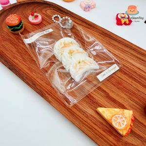 May include: A wooden serving tray displays miniature food items. A clear plastic bag contains three white, cloud-shaped items with the text "Love is the anger." Other items include a miniature burger, a pink pastry, and a slice of pie.