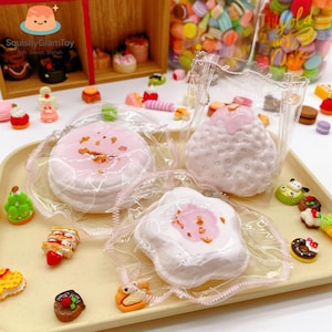May include: A selection of miniature food toys, including three squishy desserts in clear packaging. The image showcases a variety of colourful, detailed miniature food items, such as cakes and macarons, arranged on a tray.