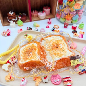May include: A collection of miniature food toys, including slices of toast, cakes, and cookies. The toast slices are packaged in clear plastic. Other miniature desserts are arranged on a tray and in a jar. The toys are colorful and detailed.