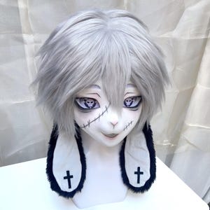 May include: A white bunny mask with gray hair and large, expressive eyes. The mask features stitched details and black crosses on the inner ears. The overall design has a spooky, yet cute aesthetic.