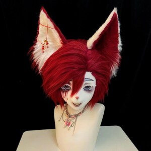May include: A red and white fox ear headdress with a matching wig. The ears are fluffy with red fur and white tips. The face is painted with detailed eyes and a pink nose. A silver chain with a pink butterfly pendant completes the look.