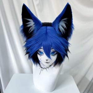 May include: A blue and black furry fox ear headpiece with matching blue wig hair. The headpiece is on a white mannequin head. The mannequin has blue eyes and a silver necklace.