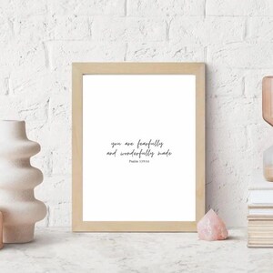 Puede incluir: Una impresión enmarcada con el texto "you are fearfully and wonderfully made" en escritura negra. El marco es de madera clara, y la impresión se muestra sobre una superficie blanca con objetos decorativos.