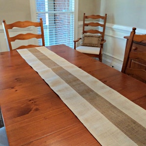 May include: A wooden dining table with a burlap and white striped table runner. The table is set with two chairs and a side table.