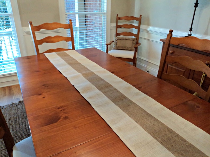 May include: A wooden dining table with a burlap and white striped table runner. The table is set with two chairs and a side table.
