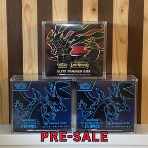 May include: Three Pokémon Elite Trainer Boxes in clear display cases. The top box is black and red with gold accents and the text "Lost Origin". Two blue boxes below feature a dragon graphic and the text "Phantasmal Flames". The word "PRE-SALE" is at the bottom.