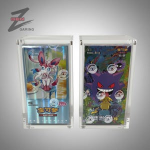Può includere: Due custodie espositive in acrilico trasparente contenenti bustine di carte collezionabili Pokémon. La bustina a sinistra mostra Sylveon con finitura olografica, mentre quella a destra presenta Gengar e Pikachu con grafiche colorate.