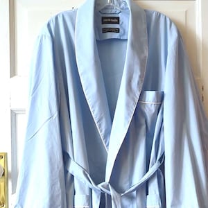 May include: A white ceramic mug with a black handle and the text "But First, Coffee" in a bold, black font. The mug is set against a neutral background, highlighting its simple design.