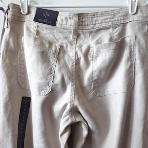 May include: Beige trousers featuring a high waistband with belt loops, two large patch pockets on the back, and a visible brand tag reading YND TROUSER / 8. The garment is displayed on a white hanger with attached retail tags and branding.